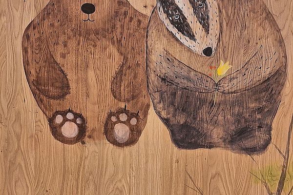 Gemalter Bär und Dachs nebeneinander auf Holz, mit Schmetterling und gelber Blume