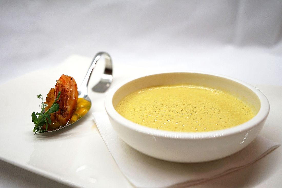 Cremige Suppe mit Garnele auf Löffel und frischer Kräutergarnitur auf weißem Teller