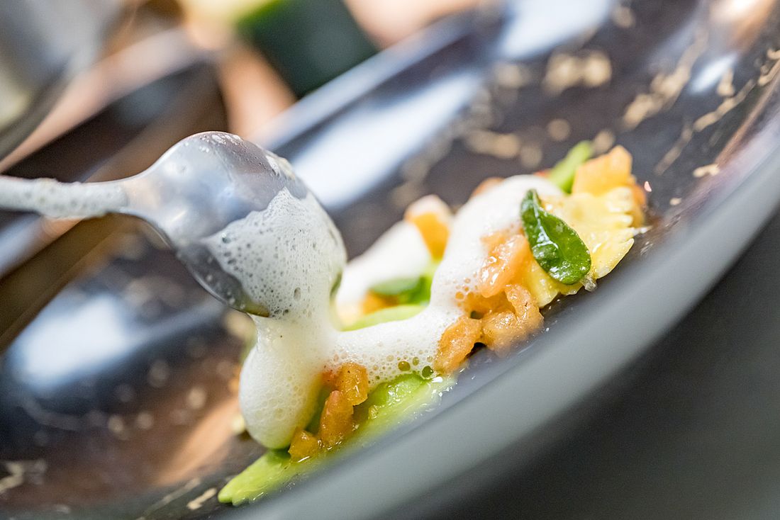 Gourmetgericht mit Gemüse, Schaum und feinen Kräutern kunstvoll angerichtet auf dunklem Teller