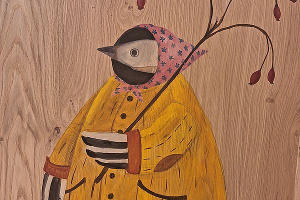 Gemalter Vogel mit gelbem Mantel und Kopftuch hält Zweig mit Hagebutten auf Holz