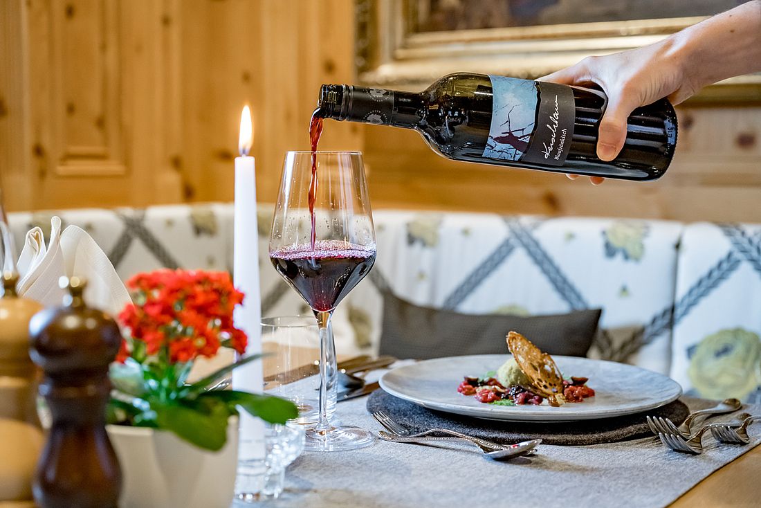 Rotwein wird am festlich gedeckten Tisch neben einer Gourmet-Vorspeise eingeschenkt