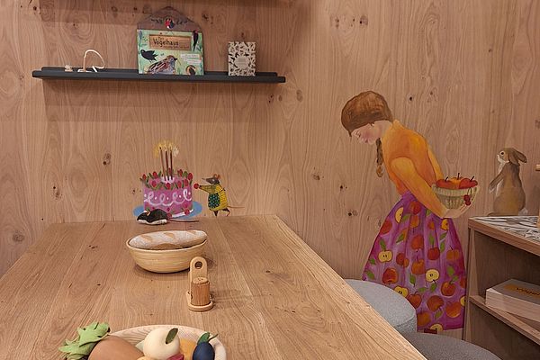 Kindertisch mit Spielgemüse, Wandbild eines Mädchens und Regalen mit Kinderbüchern
