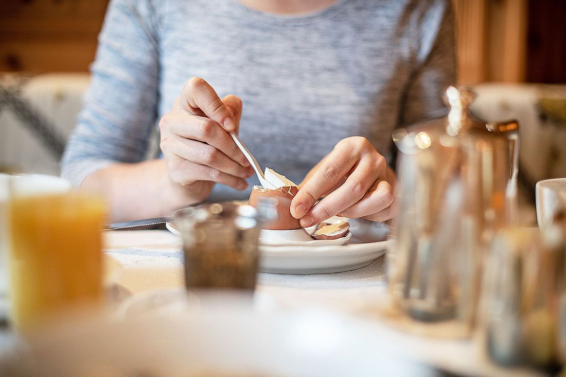Person löffelt ein weichgekochtes Frühstücksei an einem gedeckten Tisch