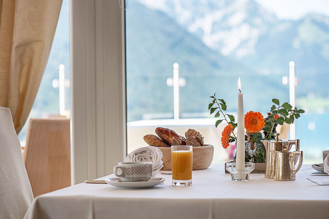 Frühstückstisch mit Gebäck, Saft und Kerze vor Panoramafenster mit Bergblick