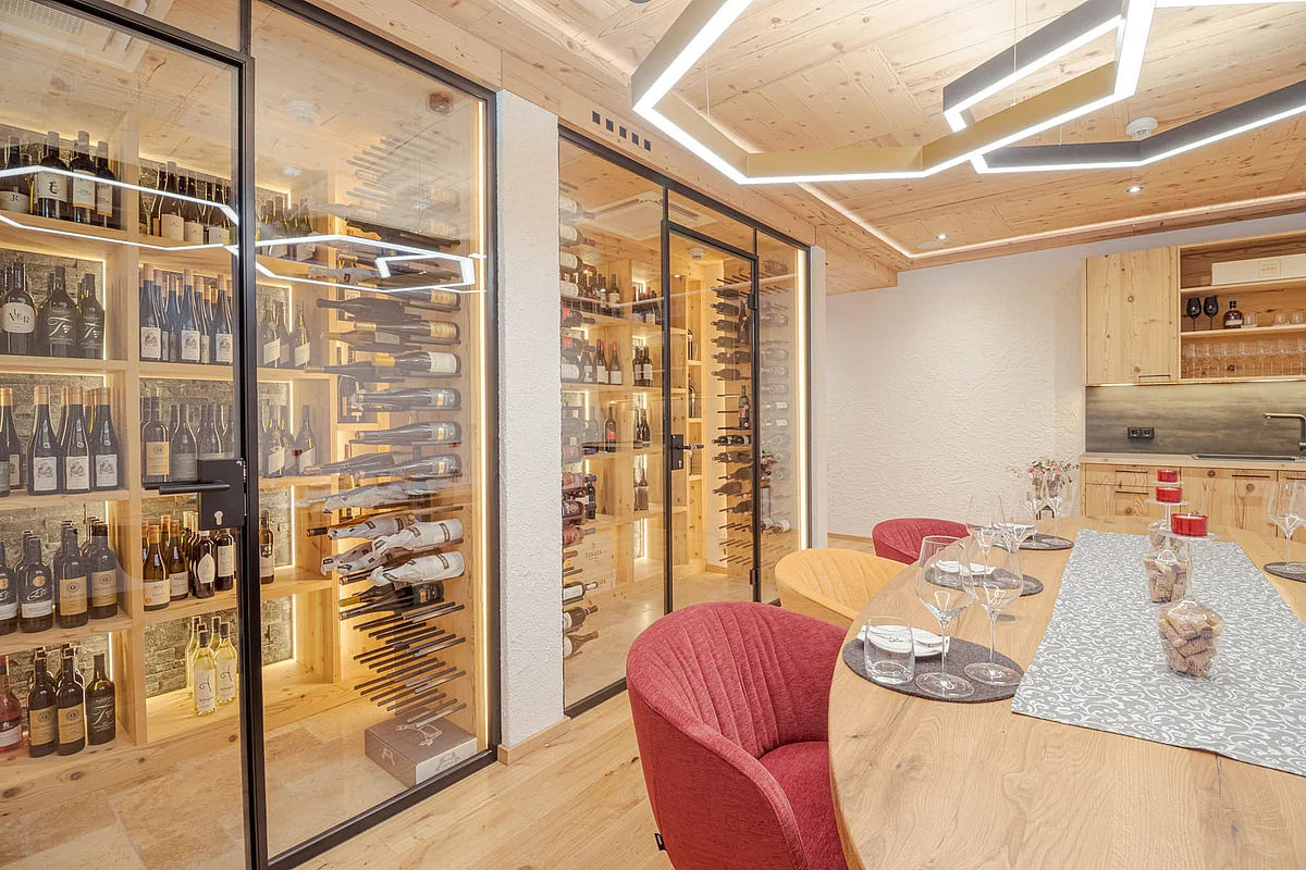 A modern dining area featuring a long wooden table, colorful chairs, and a walk-in wine cellar