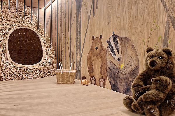 Spielbereich mit Kuschelbär, Weidenhütte und Waldbewohner-Wandmalerei auf Holz