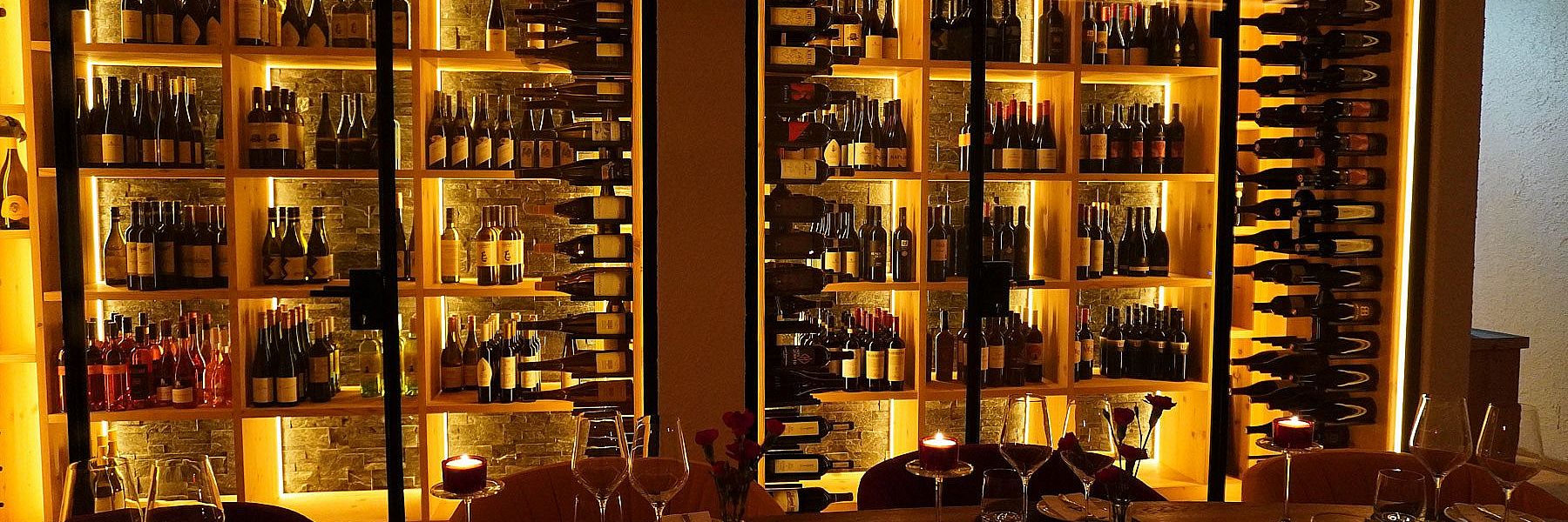 Blick auf beleuchtete Weinschränke hinter dem gedeckten Tisch im Weinkeller