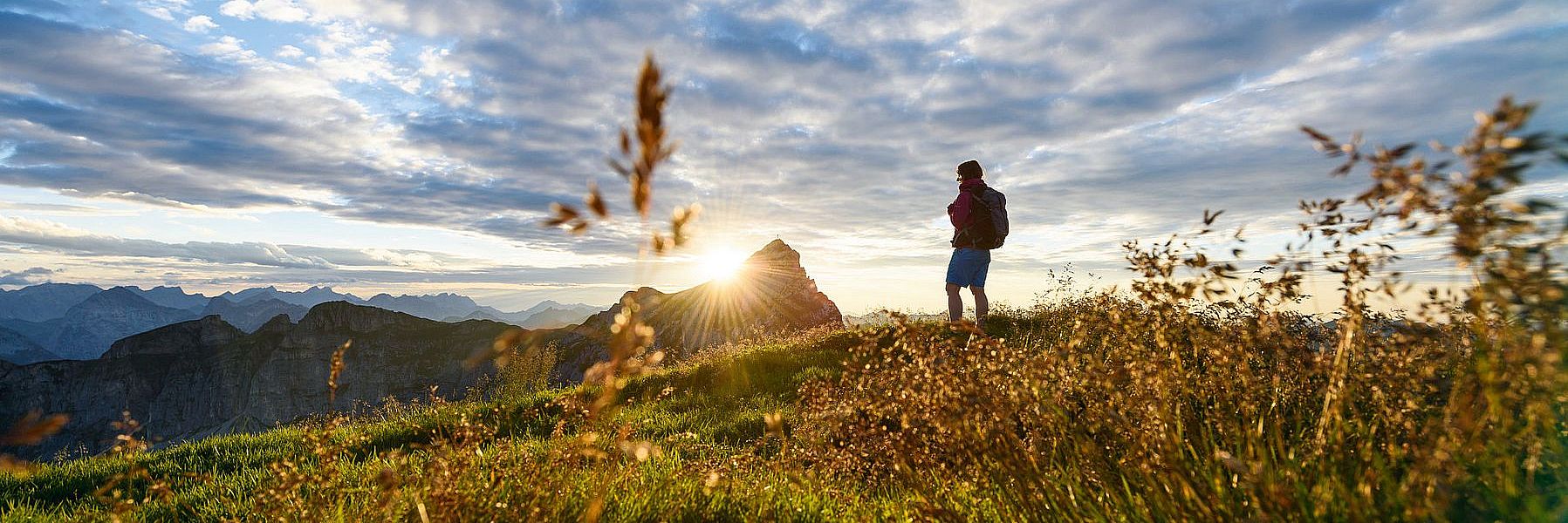 Mann bei einer Wanderung auf einer Wiese in den Bergen im Sommer bei Dämmerung